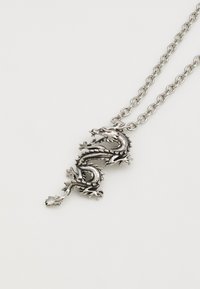 Pingente de dragão prateado numa corrente, design detalhado com escamas e garras, apresentando uma textura suave e características intrincadas.