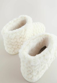 Witte pantoffels van kunstbont met een gestructureerd, doorgestikt patroon, afgerond design en een zachte, pluche binnenkant. Crèmekleurige zool voor binnenshuis gebruik.