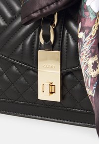 Sac à main en cuir matelassé noir avec une fermeture en métal doré. Dispose d'une écharpe décorative aux couleurs vives et aux motifs floraux attachée.