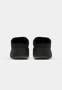 Sorte joggesko med en glatt tekstur, polstret bakstykk, og gummisåle. Har et minimalistisk design med stikkede detaljer.