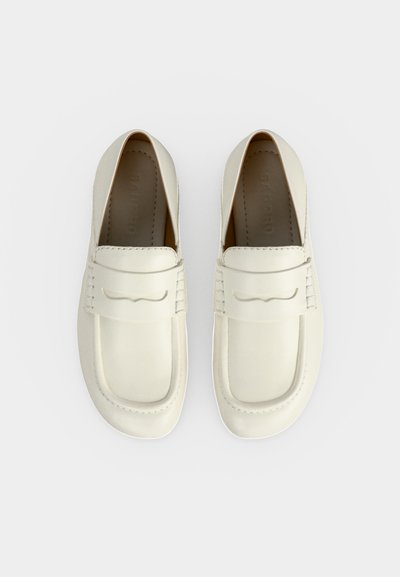 Ζευγάρι κρεμ μοκασίνια χωρίς κορδόνια με στρογγυλεμένα τετράγωνα δάχτυλα και διακοσμητικό ράψιμο σε λευκό φόντο.