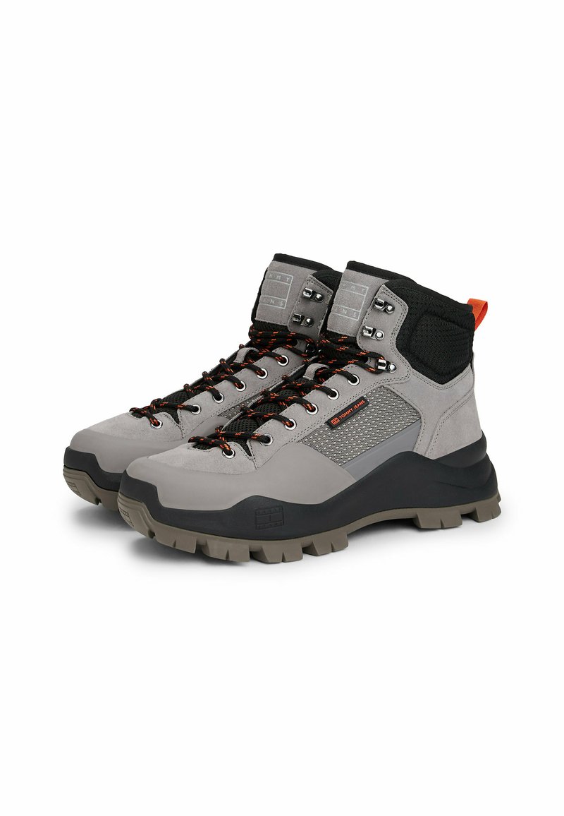 Graue Wanderschuhe mit einem Obermaterial aus Wildleder und Mesh, schwarzem Kragen, orangefarbenem Akzent und robustem grauem Profil. Mit Metallösen und Schnürsenkeln ausgestattet.
