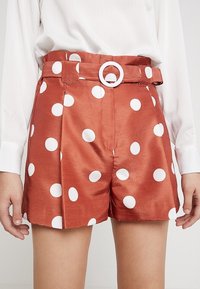 Kovově hnědé šortky s vysokým pasem vyrobené z hedvábného materiálu, s bílými puntíky, páskem s kulatou sponou a skládáním v přední části.