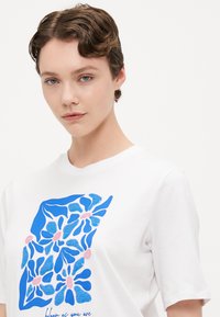 Korte mouwen witte katoenen t-shirt met een blauwe bloemenprint met roze accenten en tekst, ronde halslijn en een relaxed fit.