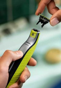 Rasoio Philips OneBlade con impugnatura verde texturizzata e corpo argentato. Un attacco con lama nera è tenuto sopra il dispositivo.