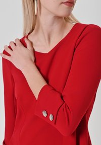 Rode top met lange mouwen in rekbare stof, voorzien van een ronde halslijn en zilveren sierknopen op de manchetten. Gladde textuur en een aansluitend model.