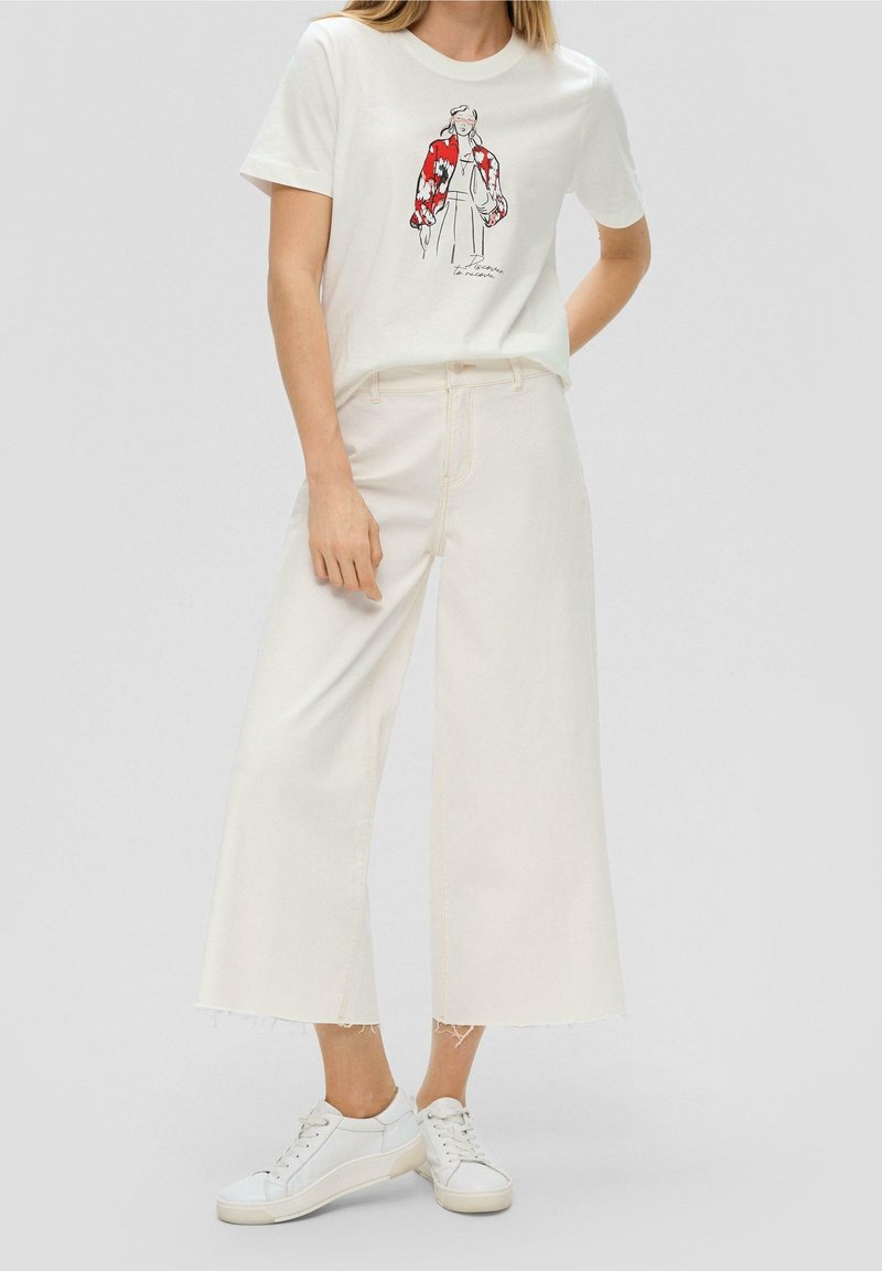 Hvid grafisk t-shirt med en rød og sort illustreret figur, parret med højhalset hvide cropped jeans og hvide sneakers.
