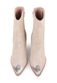 Un par de botas de ante beige hasta el tobillo con punteras afiladas y tapas decorativas de metal plateado, exhibidas una al lado de la otra sobre un fondo blanco.