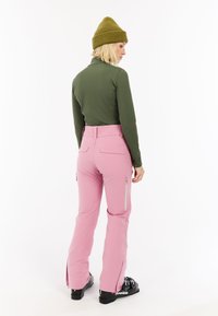 Groene lange mouw shirt, roze skibroek met ritszakken, zwarte skischoenen en een groene gebreide beanie. Gladde stof, aansluitend ontwerp.
