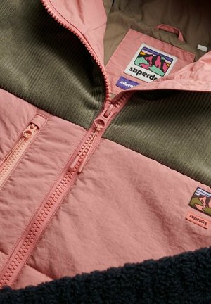 Veste zippée rose et verte avec un tissu texturé, une section en velours côtelé et une étiquette de marque avec un design de montagne.