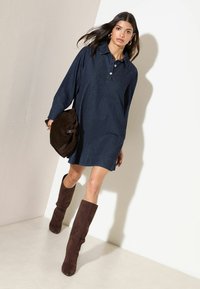 Tumesinises värvitoonis teksariidest särk-kleit, millel on krae ja nööpidega sulgemine, kombineeritud pruunide seemisnahast põlvikutega ja sobiva pruuni kotiga.