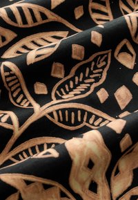 Tela negra con un diseño detallado que presenta hojas beige cremosas y formas geométricas, mostrando una textura suave y colores contrastantes.