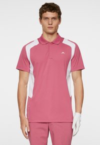 Rosa pikétröja med vita sidopaneler och en logo på bröstet; korta ärmar, krage och en slät textur.