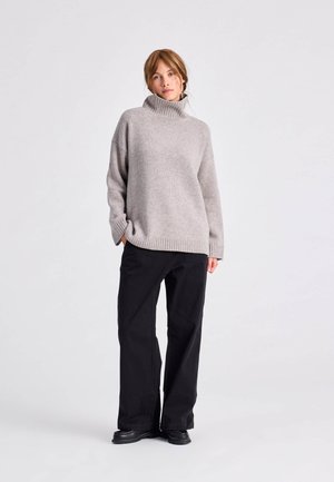 Pull en maille épaisse gris clair avec un col en côte haut, associé à un pantalon large noir et des bottes à plateforme noires. Texture douce, coupe décontractée.