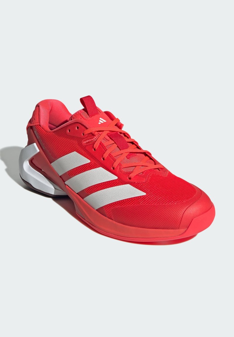 Chaussure de sport rouge avec tige en maille, trois accents en stripes blancs, et une semelle rembourrée. Présente une forme de bout arrondi et des surfaces texturées.