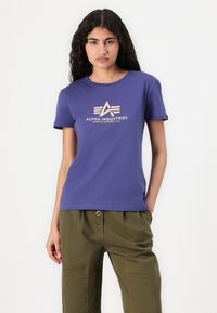 Violet medvilninis marškinėliai su apvalia iškirpte, į centrą krūtinės yra spausdinamas šviesiai smėlinės spalvos logotipas ir tekstas.