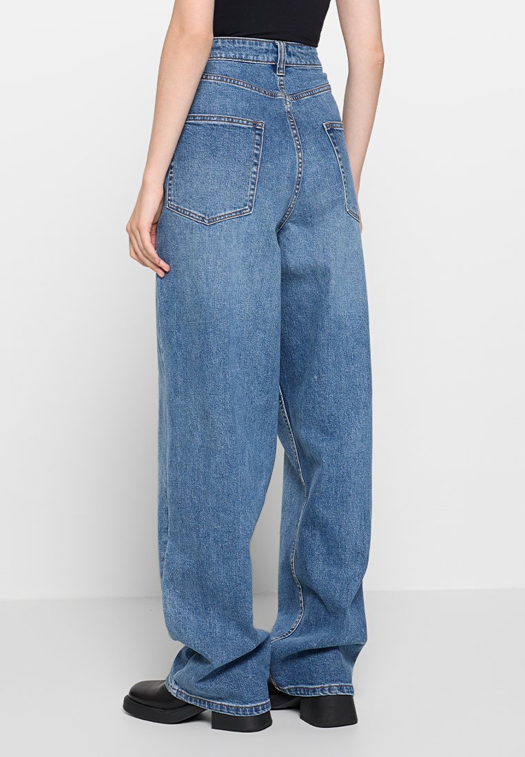 Jeans en denim bleu clair, taille haute et à jambes larges, dotés de deux grandes poches arrière et d'une finition soignée le long de l'ourlet.