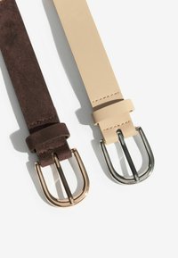 To bælter side om side: det ene i mørkebrunt ruskind med en roséguld spænde, og det andet i beige læder med en sølv spænde.