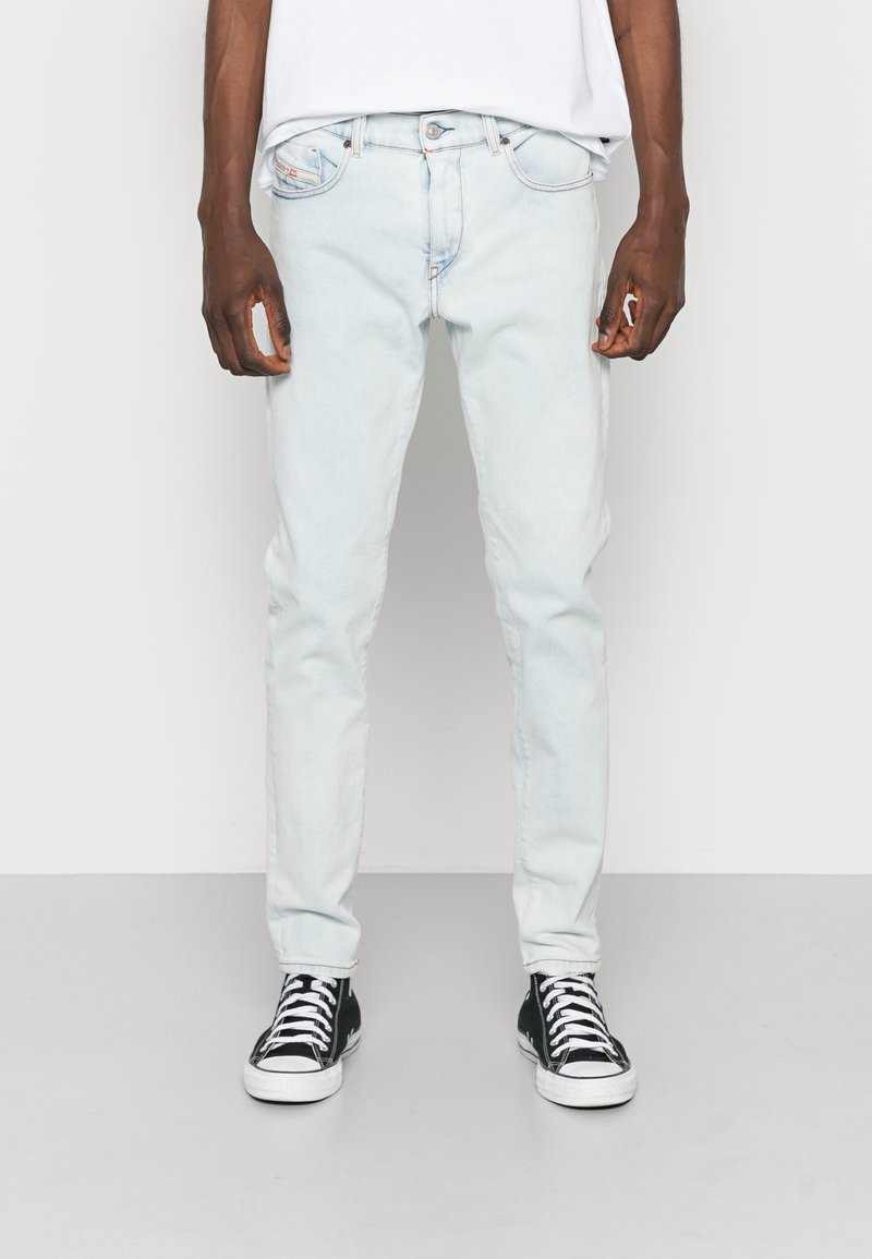 Jean en denim bleu clair avec une coupe droite, un design à cinq poches et une fermeture à boutons sur le devant. Porté avec des baskets noires et blanches.