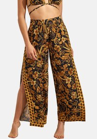 Pantalons larges à fleurs noires avec des accents dorés. Présente un motif floral, une taille élastique et des fentes latérales pour le confort et le style.
