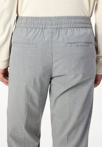 Pantalon gris avec une texture lisse, une taille élastique et deux poches arrières. Le tissu présente un motif chiné subtil.