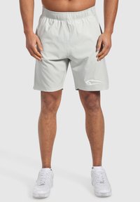 Pantalones cortos atléticos grises claros con cinturilla elástica, bolsillos laterales, textura suave y un logo sutil cerca del dobladillo. Se llevan con zapatillas blancas.