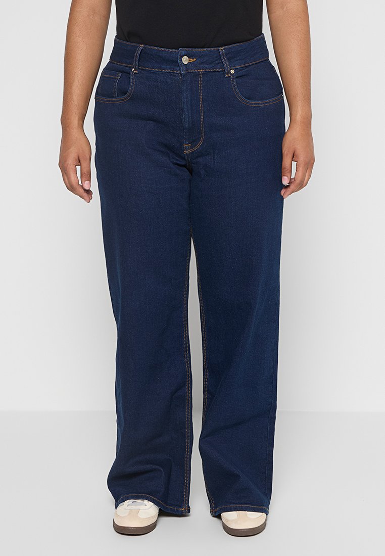 Jean en denim bleu foncé avec une coupe relaxée, comportant deux poches avant, des coutures contrastantes et une fermeture à bouton à la taille.