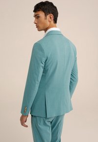 Blazer color azul verdoso fabricado con una tela texturizada, que presenta una abertura simple en la parte posterior, con botones dorados en los detalles de los puños. Ajuste entallado.
