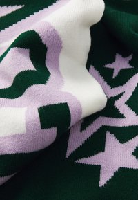 Strickstoff in Grün, Weiß und Flieder mit Stern- und Wellenmustern. Strukturiert, weich, mit ausgeprägten kontrastierenden Farben und Formen.