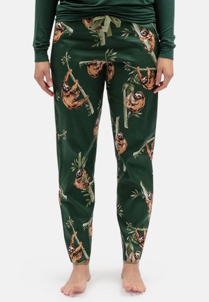 Groene pyjamabroek met een aantrekkoord in de taille en een herhalend patroon van luiaarden die aan takken hangen. Blote voeten zichtbaar.