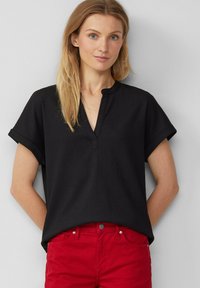 Zwarte top met korte mouwen en een lichte V-hals, met een gestructureerde stof en opgerolde mouwen, gecombineerd met rode broek met een knoop en zakken.
