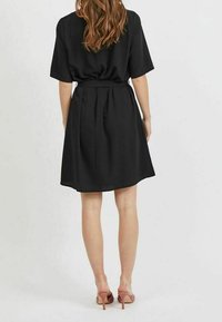 Svart kortärmad klänning med bälte i midjan, flödande kjol, mid-thigh längd, slät textur och enkel design. Matchas med rosa klackar.