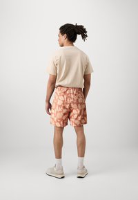 Beige cotton t-shirt and orange patterned shorts with leaf designs, elastic waistband, paired with light-colored athletic shoes.