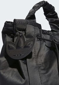 Černá látková taška s texturovaným povrchem, která má stahovací šňůrku a převelký černý gumový štítek s třemi pruhy.