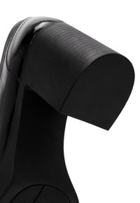 Il tacco di una scarpa nera con tacco alto presenta una finitura lucida, una texture ondulata e una forma arrotondata, con una suola in gomma solida per una buona aderenza.