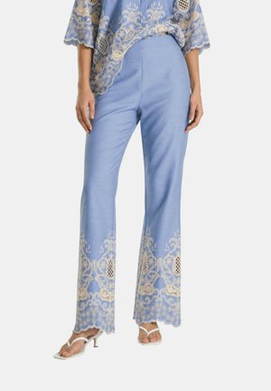 Pantaloni azzurri chiari con ricamo in pizzo beige sull'orlo, indossati con top abbinato e sandali bianchi con tacco su una persona in piedi.