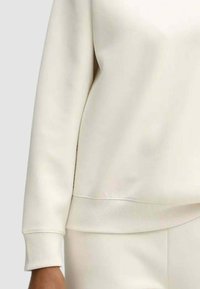 Felpa color crema con polsini e orlo a coste, caratterizzata da una texture liscia e un design semplice. Non sono visibili motivi o accenti particolari.