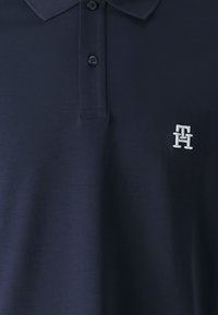 Námořnická modrá polo tričko vyrobené z měkké bavlny, s límcem, dvouknoflíkovou légou a malým vyšitým logem na levé hrudi.