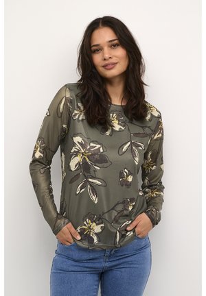 Långärmad olivgrön topp med blommönster i svart och gult. Slät textur, rund halsringning och avslappnad passform. Denimjeans bärs.