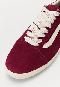 Sneaker din suede burgund cu șireturi albe și accente laterale. Vârf rotund cu o talpă plată din cauciuc și suprafață texturată. Elemente de design curate.