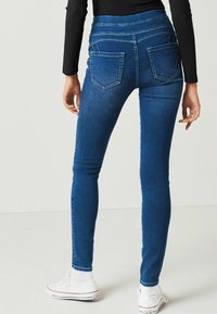 Tmavě modré skinny džíny s vysokým pasem, se zadními kapsami a kontrastním prošíváním, kombinované s bílými teniskami.