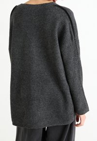 Tmavě šedý žebrovaný svetr s volným střihem, který má široký výstřih a výrazné švy na ramenou a po stranách.