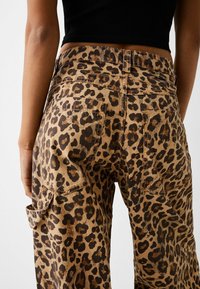 Cargobroek met luipaardprint in bruin en zwart, met een hoge taille, twee achterzakken en zichtbare stiksels.