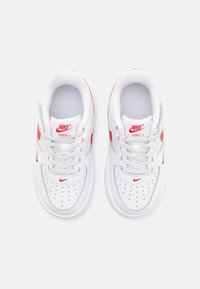 Valged Nike tossud punaste aktsentidega, millel on siledast nahast ülaserv, ümar varvas, perforatsioonid ja lamedad paelad. Kujundatud igapäevaseks kandmiseks.
