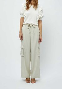 Avslappnad outfit med en vit topp med volangärmar och beige vida cargobyxor med sidfickor, knyt i midjan och öppna skor.