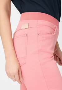 Rosa Hosen mit einem dehnbaren Bund, ausgestattet mit Gesäßtaschen und einem kleinen Stoffetikett. Glatte Textur mit maßgeschneiderten Nähten und Details.