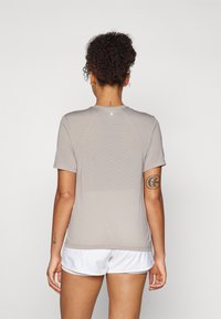 Camiseta atlética gris claro de manga corta y cuello redondo. Presenta una tela texturizada, un logo sutil en la parte posterior y un diseño ajustado.