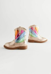 Botas de tobillo metálicas doradas con rayas de satén multicolores en rosa, naranja, azul, verde y una suela de goma marrón.