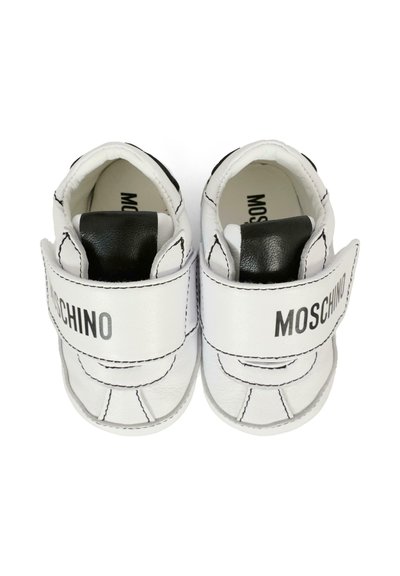 Scarpine per bambini piccolissimi in pelle bianca, con dettagli neri, cinturini in Velcro e cuciture in contrasto. Logo "Moschino" stampato sul cinturino.
