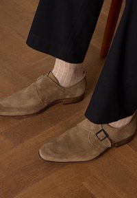 Tan suède schoenen met een gladde afwerking, een gestikt design en een gespaccent. Draagt met lichte geribbelde sokken en donkere broeken.